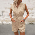 Woman wearing a beige romper against a textured wall.
