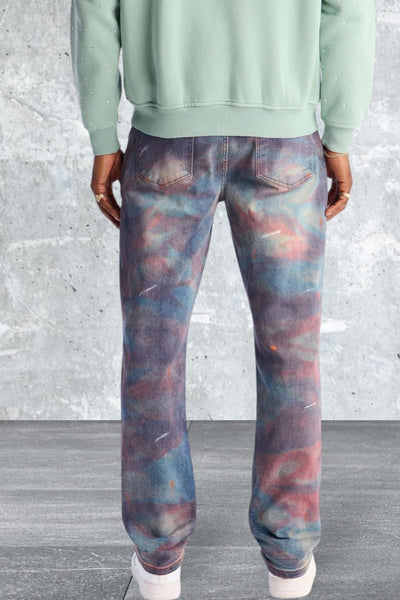 Person wearing a light green sweatshirt and multicolored pants against a gray concrete wall.