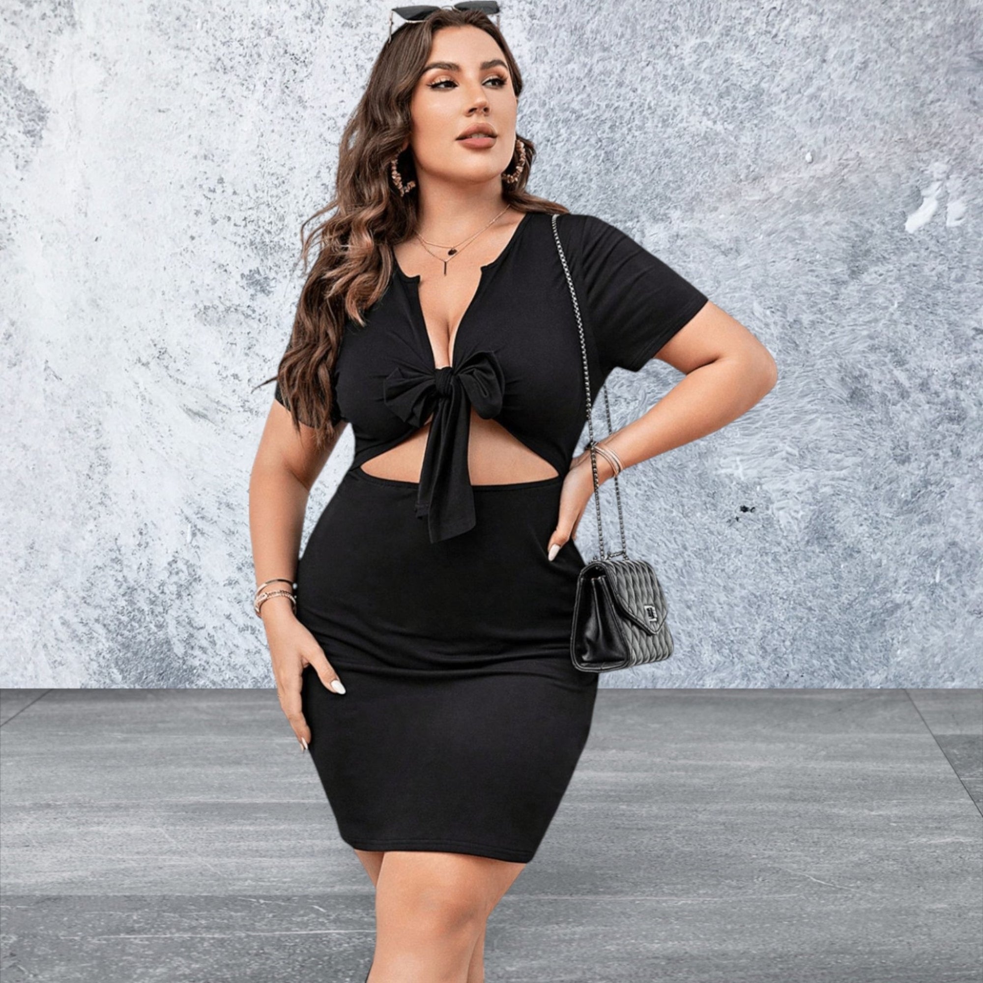 Woman wearing a black dress with cut-out design against a textured gray wall.