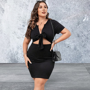 Woman wearing a black dress with cut-out design against a textured gray wall.
