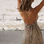 Person wearing a leopard print dress with criss-cross straps against a textured wall.